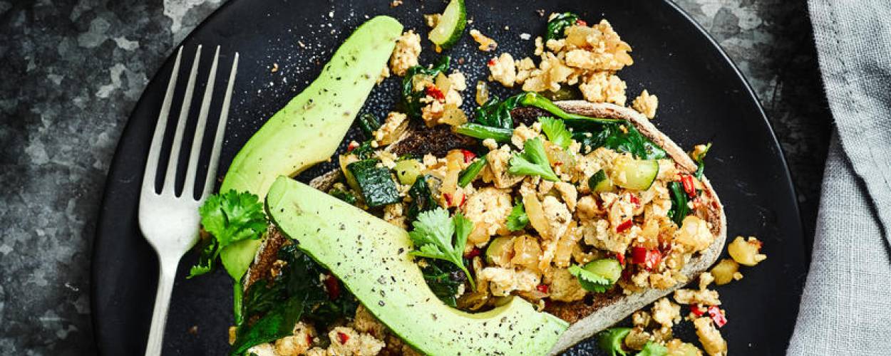 Tofu Scramble mit Avocado auf schwarzem Teller