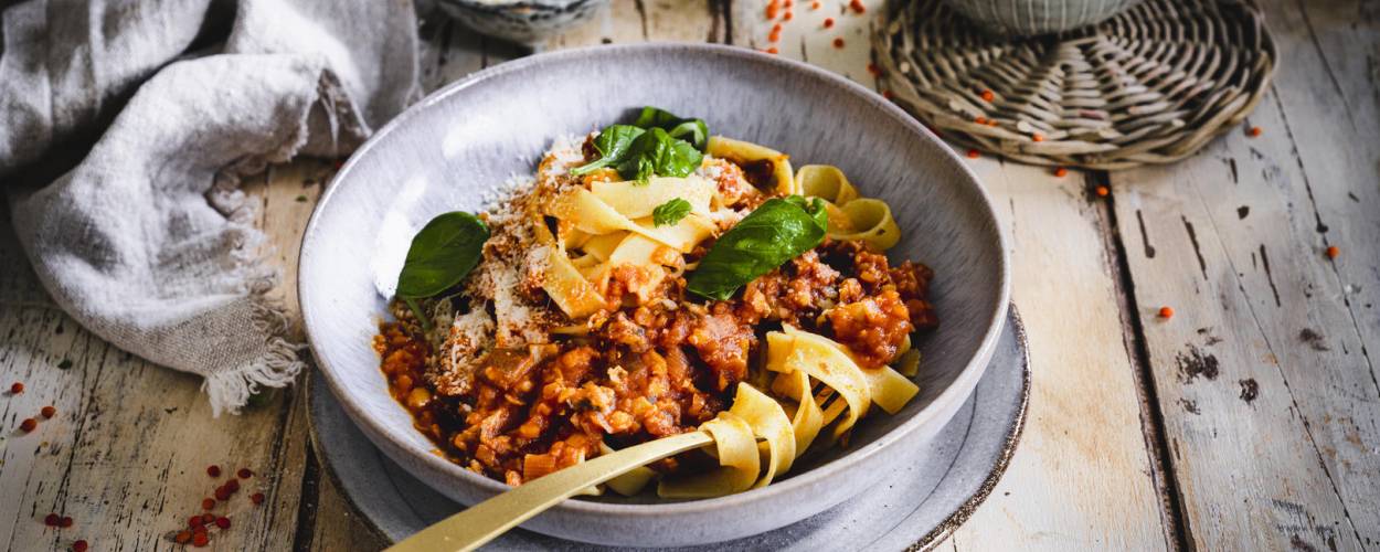 Bandnudeln mit Linsen in roter Soße auf tiefem grauen Teller