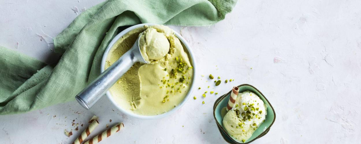 Pistazieneis in Schüssel mit Eislöffel, grünem Handtuch und Waffelröllchen