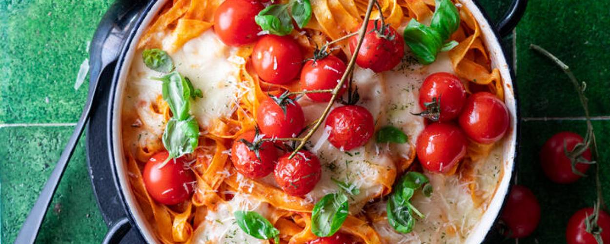 Nudelauflauf mit Tomaten, Basilikum und Parmesan auf grüner Überfläche in runder Auflaufform