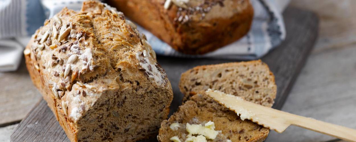 Brotlaib angeschnittten mit Butter auf Holzbrett mit Messer