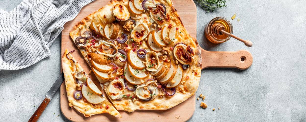 Flammkuchen auf Holzbrett mit Honig und Kräutern