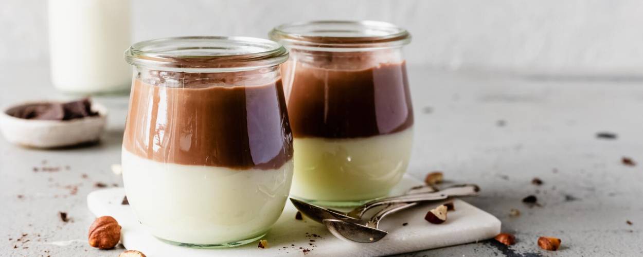 Dunkle und helle Creme im Glas mit Milch und Nüssen auf Tablett