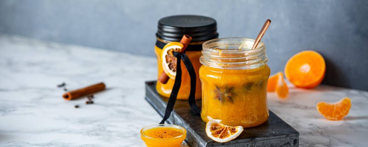 Orange Marmelade mit Glitzer in Glas mit Mandarinen und Zimt