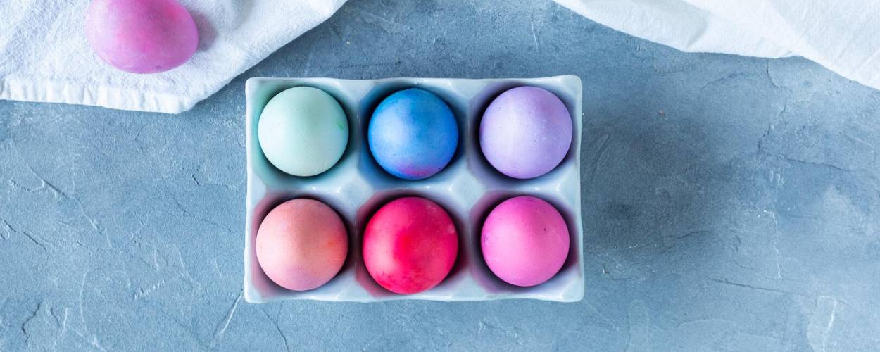 Bunte Eier in Karton und auf weißem Tuch