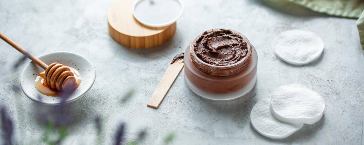 Braune Maske in Glasgefäß mit Holztiegel, Wattepads und Honig