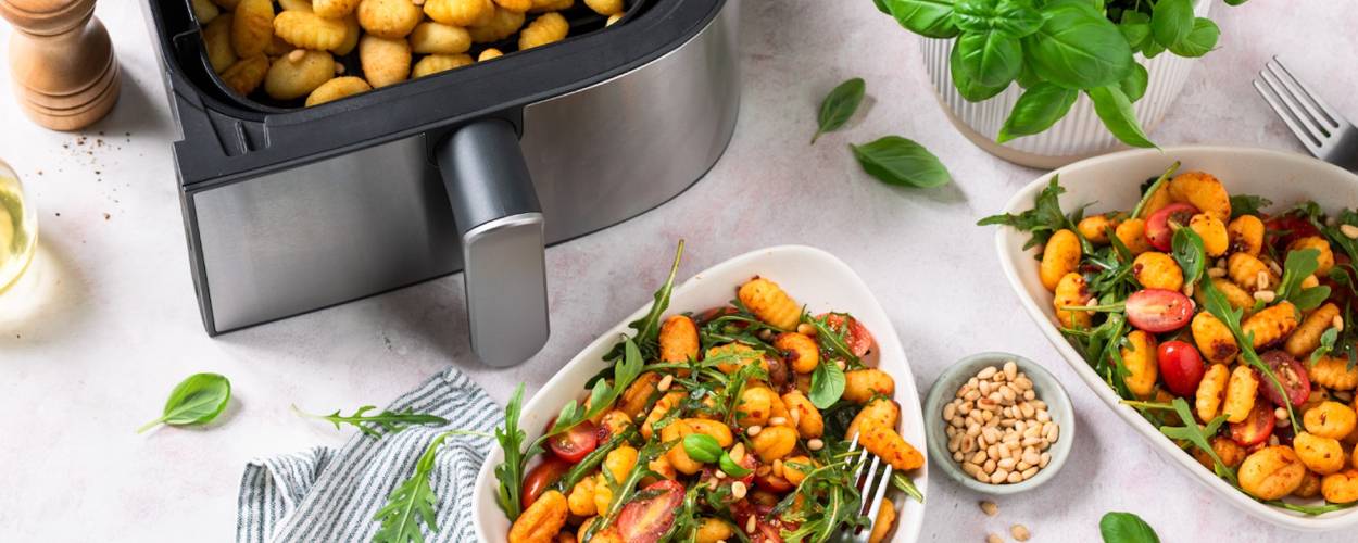 Gnocchi mit Ruccola und Tomaten auf weißen Tellern, daneben der Airfryer mit Gnocchi in der Schublade