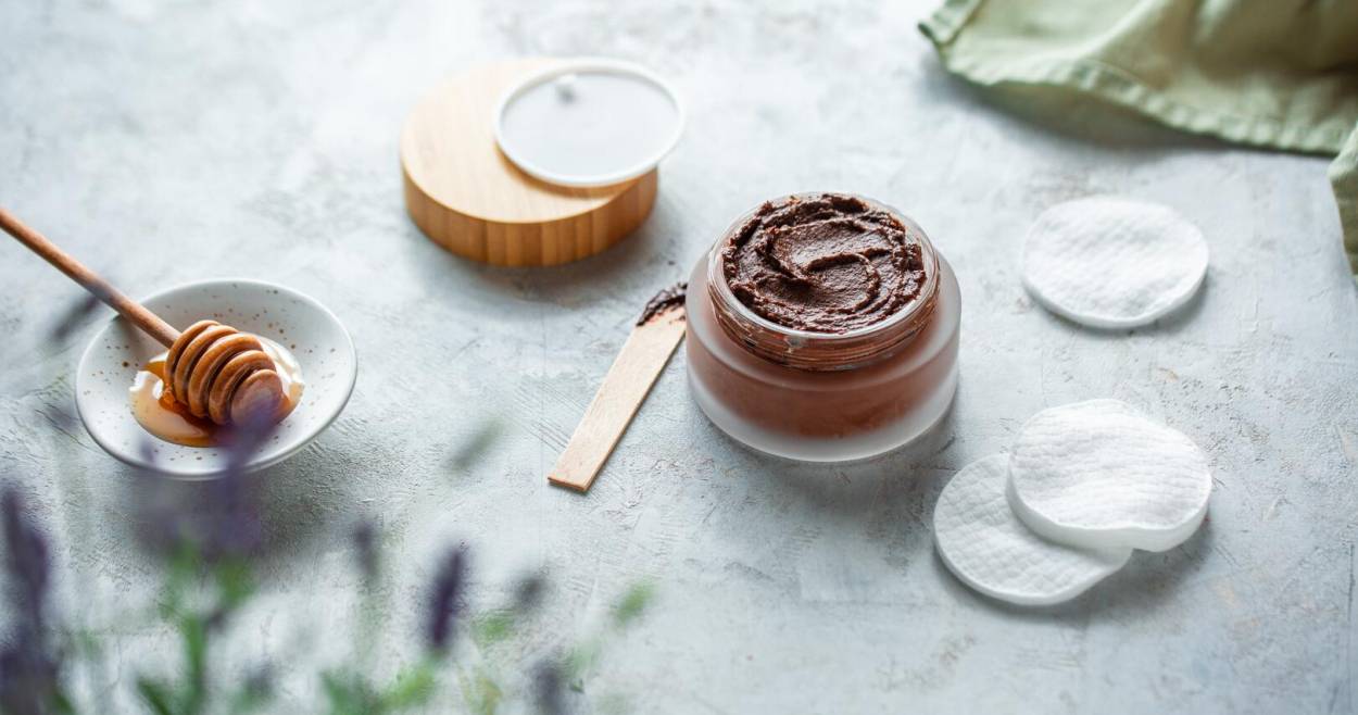 Braune Maske in Glasgefäß mit Holztiegel, Wattepads und Honig