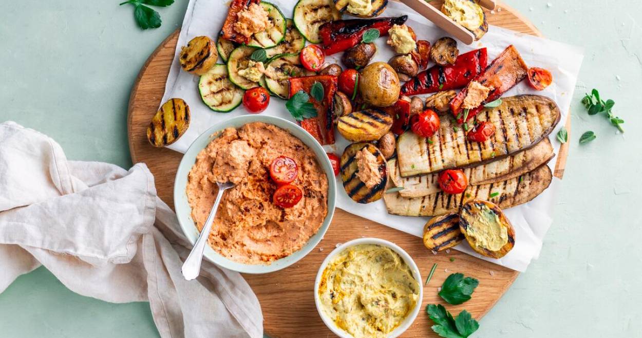 Grillgemüse und Dips auf rundem Holzbrett mit Grillzange aus Holz