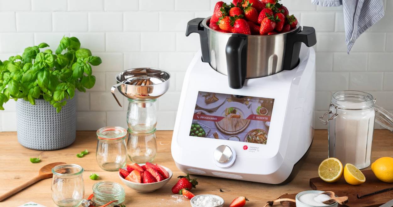 Der Monsieur Cuisine auf einer Arbeitsplatte aus Holz, im Mixbehälter sind Erdbeeren, die über den Rand schauen
