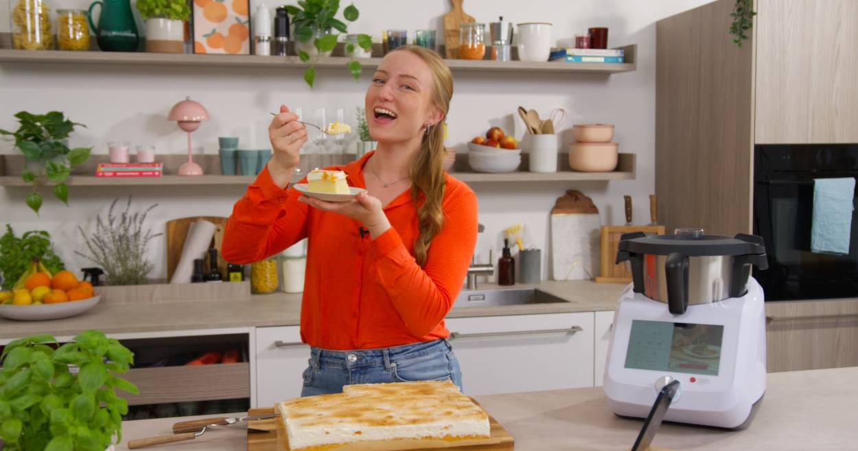 Isy isst ein Stück Kuchen und steht neben dem Monsieur Cuisine