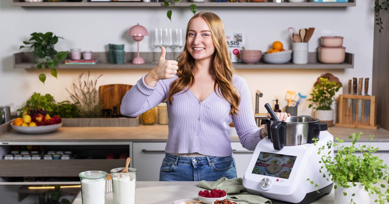Junge Frau in einer Küche neben dem Monsieur Cuisine, hebt den Daumen