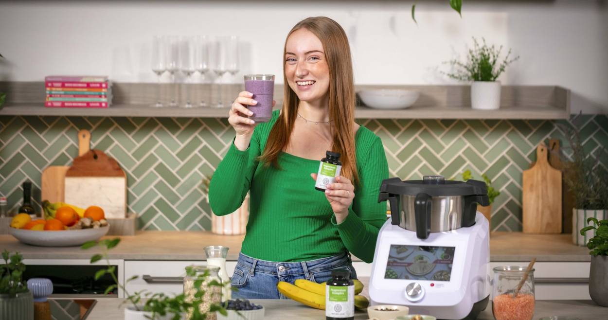 Junge Frau in einer Küche mit Monsieur Cuisine, in einer Hand ein Blaubeer-Shake