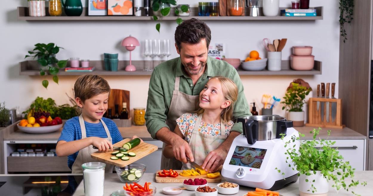 Ein Mann und zwei Kinder in einer Küche mit Monsieur Cuisine beim Gemüse schneiden