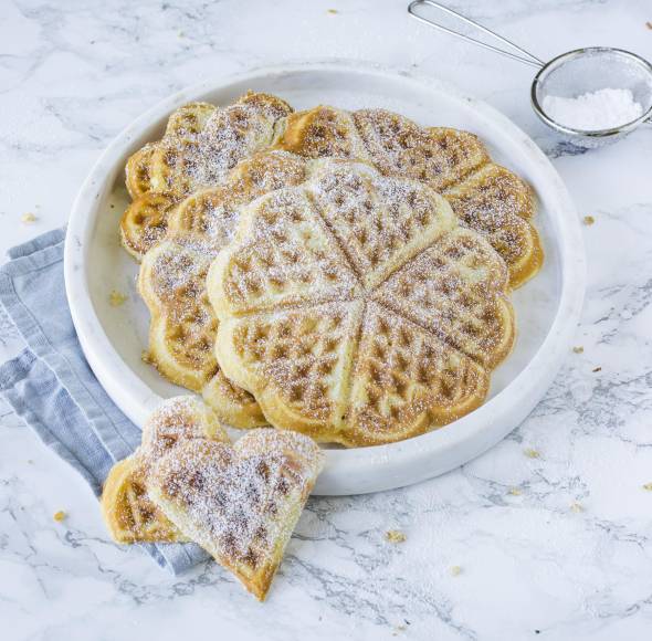 Waffeln in Herzformen auf einem Teller mit Puderzucker überstreut