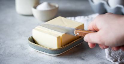 Butter in einer Butterschale wird mit einem Messer in Scheiben geschnitten.