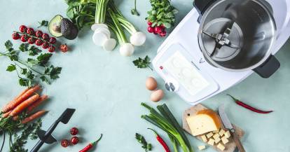 Der Mixtopf des Monsieur Cuisine von oben, umgeben von gemüse und Kräutern