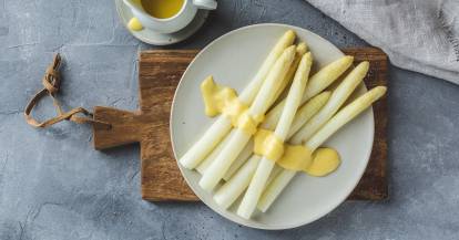 Weiße Spargelstangen mit Sauce hollandaise auf rundem weißen Teller