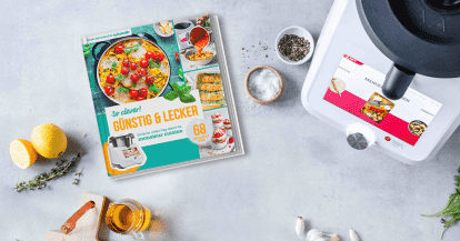 Neues ZauberMix-Kochbuch "Günstig & Lecker" liegen neben dem Monsieur Cuisine und umringt von Zutaten auf einer Arbeitsplatte
