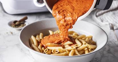 Cremige Tomatensoße wird aus dem Mixtopf auf einen Teller Nudeln gegeben.