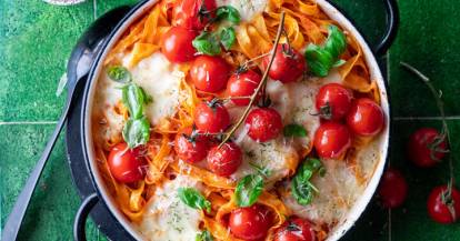 Nudelauflauf mit Tomaten, Basilikum und Parmesan auf grĂŒner ĂberflĂ€che in runder Auflaufform