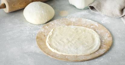 Ausgerollter Pizzateig auf einem Holzbrett.