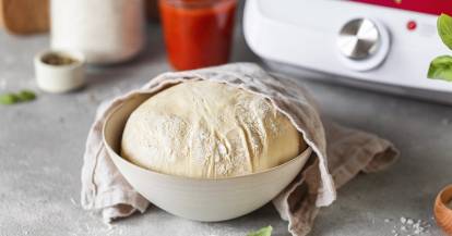 Aufgegangener Pizzateig in einer Schüssel, halb abgedeckt mit einem Küchentuch.