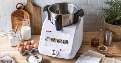 Monsieur Cuisine mit Eiern und Rezeptbüchern auf einer Arbeitsplatte.