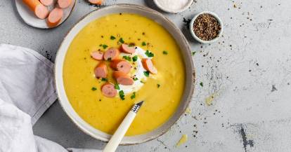 Kartoffelsuppe mit Creme und Würstchen in einer Schale mit Löffel.