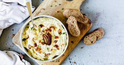 Dattel-Dip in einer Schale mit Löffel auf einem Holzbrett mit Brot