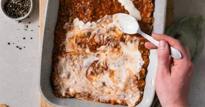 Soße wird auf eine Lasagne gegeben