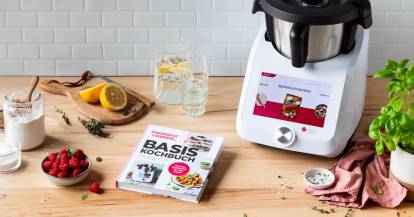 Das Basis-Kochbuch liegt auf einer Arbeitsfläche neben dem Monsieur Cuisine und einigen Zutaten.