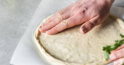 Zwei Hände glätten Pizzateig