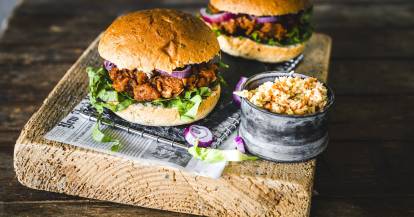 zwei Burger mit Pulled Jackfruit, daneben Krautsalat, auf einem Holzbrett