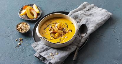 Eine Schüssel mit Kürbissuppe auf einem grauen Tuch vor blaugrauem Hintergrund
