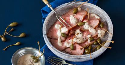 Vitello tonnato mit Kapern garniert in einer Schale auf blauem Untergrund