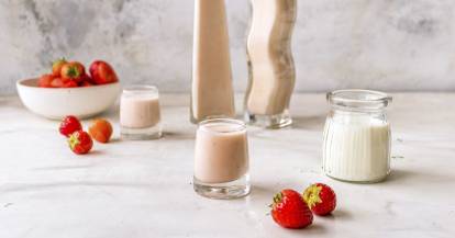 Zwei Flaschen mit cremigem rosafarbenen Likör, im Vordergrund ein Glas