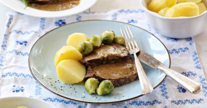 Zwei Scheiben Sauerbraten mit Kartoffeln und Rosenkohl auf hellem Teller