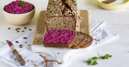 Angeschnittenes, dunkles Brot. Drei Scheiben liegen davor, eine ist mit rotem Aufstrich bestrichen.