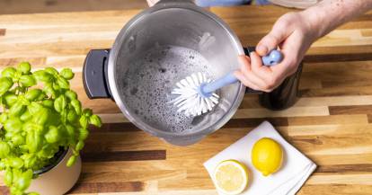Topf des Monsieur Cuisine von oben, darin Wasser mit Schaum, eine Hand hält eine Spülbürste und reinigt den Topf