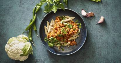 Ein Teller mit Pasta und Soße, daneben Knoblauch und Blumenkohl