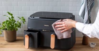 Eine Hand hält einen Lappen und wischt die Heißluftfritteuse ab