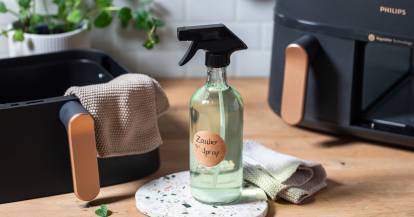 Eine durchsichtige Flasche mit Zauberspray steht vor dem Airfryer