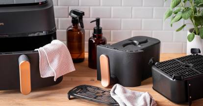 Der Philips Airfryer in Einzelteilen, daneben Lappen und Reinigungsmittel