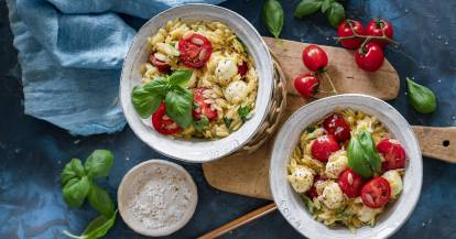 Orzo mit Tomate, Mozzarella, Basilikum in zwei Schälchen auf Holzbrettchen