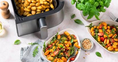 Gnocchi mit Ruccola und Tomaten auf weißen Tellern, daneben der Airfryer mit Gnocchi in der Schublade