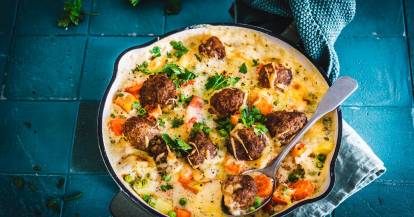 Auflauf mit HackbÀllchen in einer runden Form, von oben fotografiert. Auf blauem Untergrund