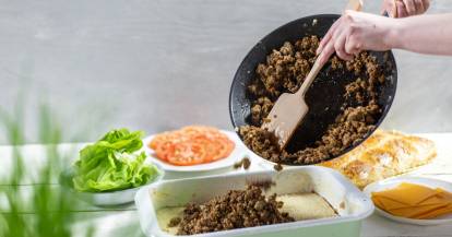 Jemand gibt angebratenes Hack aus einer Pfanne in eine Auflaufform