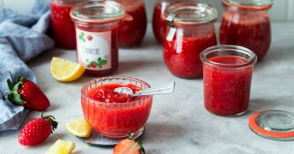 Mehrere Gläser mit roter Marmelade, daneben Erdbeeren und geviertelte Zitronen