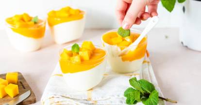 Vier Gläser mit heller Creme und einer orangefarbenen Soße, garniert mit Mango und Minzblättern